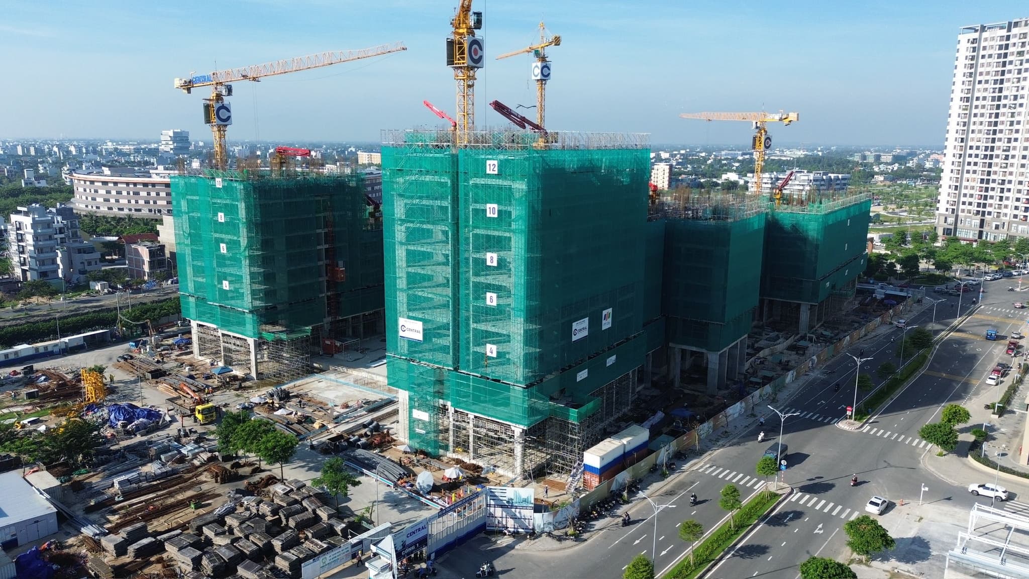 Aerial view of high-rise buildings under construction with tower cranes and green safety netting in a city.