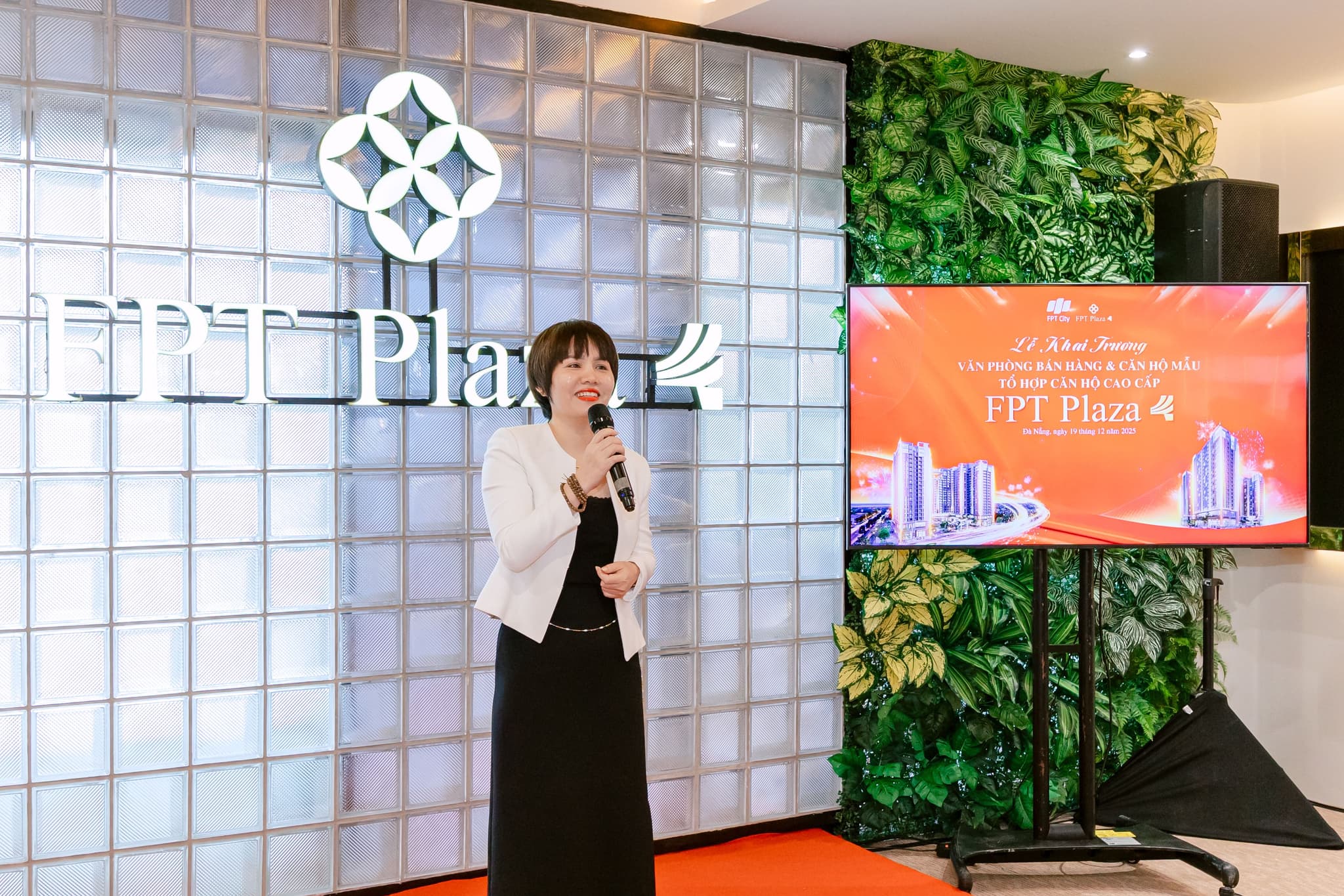 Corporate event speaker presenting at FPT Plaza, with a logo backdrop and a digital screen displaying event details.