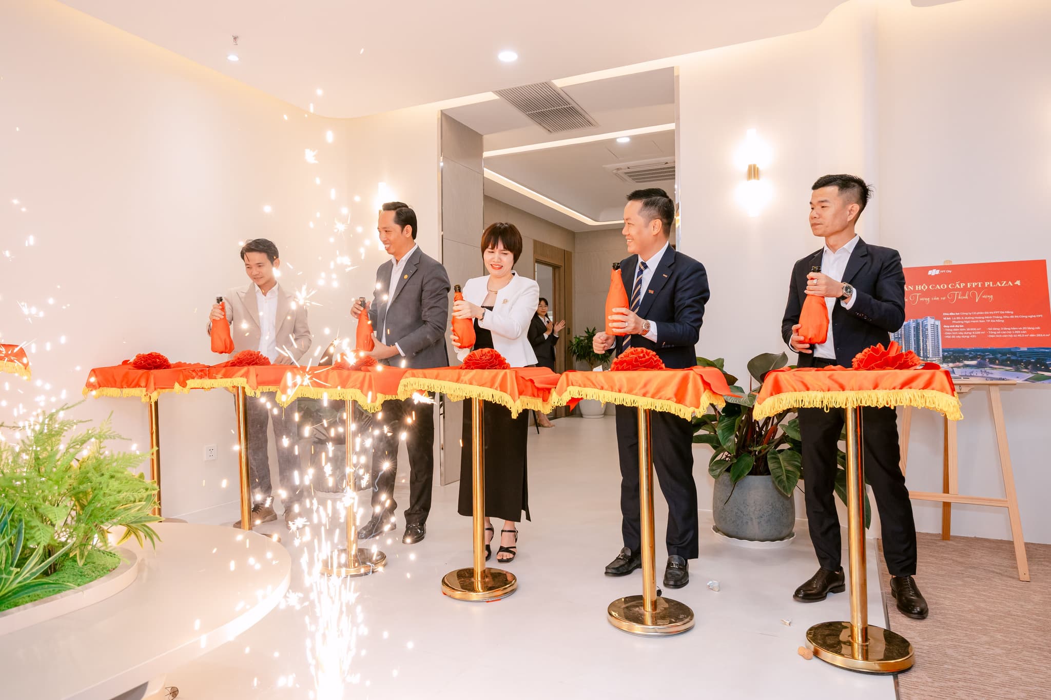 Ceremonial event with participants holding red bottles, celebrating a milestone with sparkles in a modern venue.