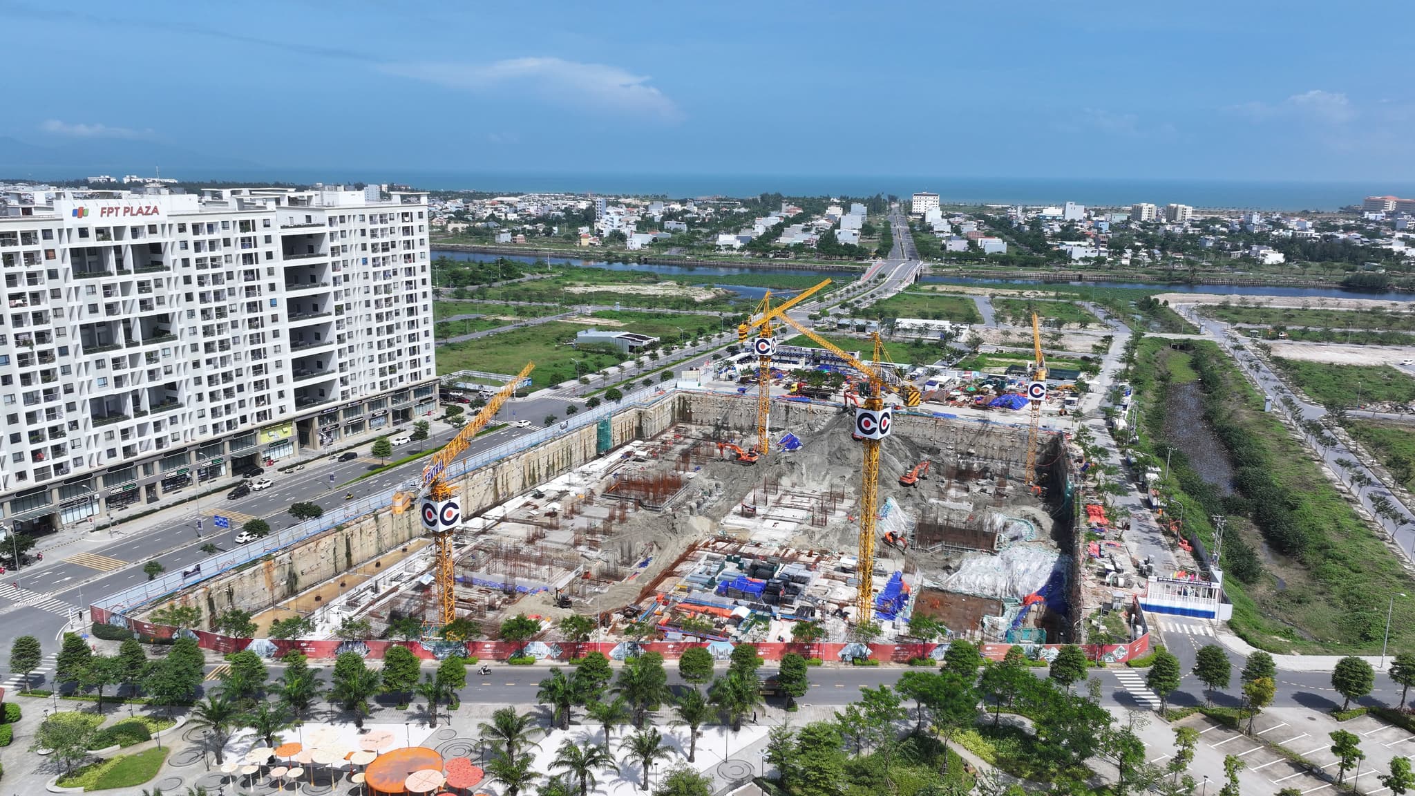 Aerial view of an urban construction site with tower cranes, high-rise apartments and landscaped roads.